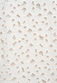 Λευκό ύφασμα με περίτεχνη κεντητική διάτρητη διακόσμηση εμπνευσμένη από λουλούδια που σχηματίζει ένα επαναλαμβανόμενο μοτίβο συνδεδεμένων σχημάτων.