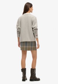 Grijze sweatshirt met geribbelde manchetten, gecombineerd met een geruite minirok in blauw, geel en zwart. Bruine laarzen tot de knie met gespsluiting.