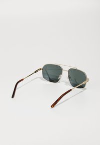 Occhiali da sole ottagonali in oro metallico con lenti grigio scuro, caratterizzati da punte delle tempie con motivo tartarugato e un design minimalista.