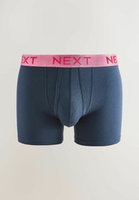 Temno modri bokserice iz raztegljive tkanine, ki imajo roza elastičen pas z odtisnjenimi besedami "NEXT" v odebeljenih črkah.