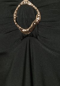 Zwart samengeplooid stof met een centrale onregelmatige gouden metalen ring die een samengetrokken designeffect creëert.