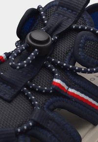 Ναυτικό μπλε σανδάλι με ρυθμιζόμενες κορδόνια τύπου bungee που διαθέτουν αντανακλαστικές κουκκίδες και μαύρη λεπτομέρεια με κλείδωμα τύπου toggle.