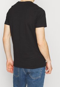 Svart bomullströja med korta ärmar och rundad halsringning. Tyget ser mjukt och slätt ut. Bärs med blå denimjeans.