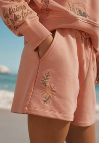 I pantaloni corti di cotone rosa presentano un ricamo di sole e foglia, con un taglio rilassato e una vita elastica per il massimo comfort.