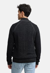 Czarny dziany sweter z teksturowanym wzorem, ściągaczami na mankietach i dolnym brzegu. Posiada wysoki kołnierz i rękawy raglanowe.