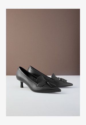 Pantofi cu toc înalt din piele neagră, cu vârf ascuțit și detaliu cu ciucuri în față. Textură netedă și design geometric al tocului.