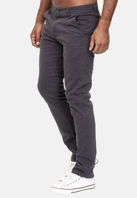 Graue, enganliegende Hose mit glatter Textur, vier Taschen-Design und Knopfverschluss, getragen mit weißen Sneakers.