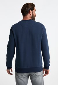 Felpa blu navy con collo rotondo, maniche lunghe e polsini a coste. Tessuto morbido con una consistenza liscia, che presenta un dettaglio di yoke posteriore arrotondato.