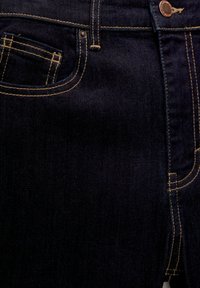 Jean en denim bleu foncé avec coutures jaunes, doté d'une poche avant, d'une fermeture à bouton métallique et d'un tissu lisse et texturé.