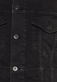 Svart denimjacka med knäppt fram, två bröstfickor och dubbelsydda sömmar. Tyget har en slät yta med en lätt glans.