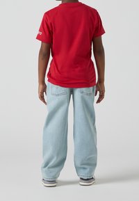 Camiseta roja de algodón con mangas cortas, combinada con jeans de mezclilla de pierna ancha en azul claro. Vista trasera que muestra detalles de costura.