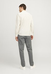 Lichtbeige gestreepte shirt met lange mouwen, relaxte pasvorm, met knoopmanchetten, gecombineerd met grijze katoenen broeken en witte sneakers.