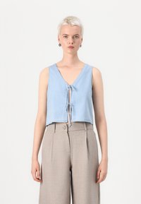 Lichtblauw cropped top met een diepe V-hals, geknoopte voorkant en brede bandjes, gecombineerd met beige op maat gemaakte high-waisted broeken.
