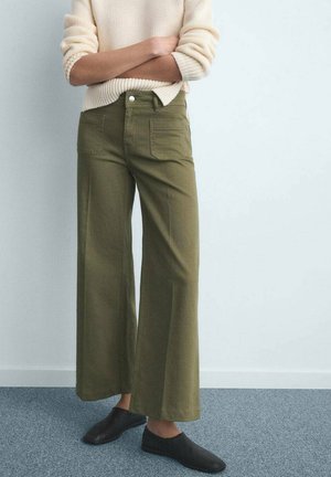 Pantalon large couleur vert olive en coton, avec poches avant et arrière, et fermeture à boutons. Associé à un pull en maille crème.