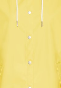 Veste de pluie jaune avec boutons en métal argenté, capuche avec cordon de serrage et texture de tissu lisse et imperméable, dotée de poches latérales.