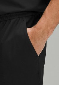 Sorte atletiske shorts med elastisk talje og sidelommer. Stofet ser glat og let ud, med synlige syningsdetaljer.