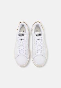 Coppia di scarpe da ginnastica Adidas Stan Smith bianche con accenti dorati sul tallone, viste dall'alto su sfondo bianco.