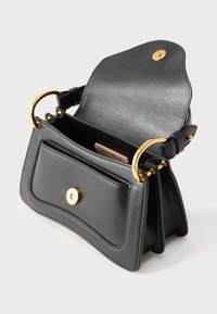 Borsa a mano in pelle nera con manici ad anello dorato, tasca frontale con bottone a pressione e patta superiore aperta che mostra l'interno con una piccola targhetta con il marchio.