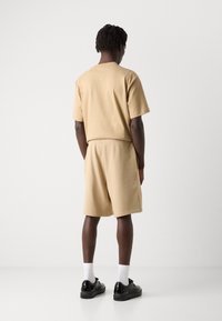 Ensemble en coton beige composé d'un t-shirt et d'un short avec une taille élastique. Baskets noires, chaussettes blanches. Design simple sans logos ni motifs visibles.
