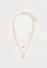 Collar de múltiples capas en oro que presenta cadenas de cuentas blancas, un acento redondo dorado y un colgante dorado con un diseño en relieve.