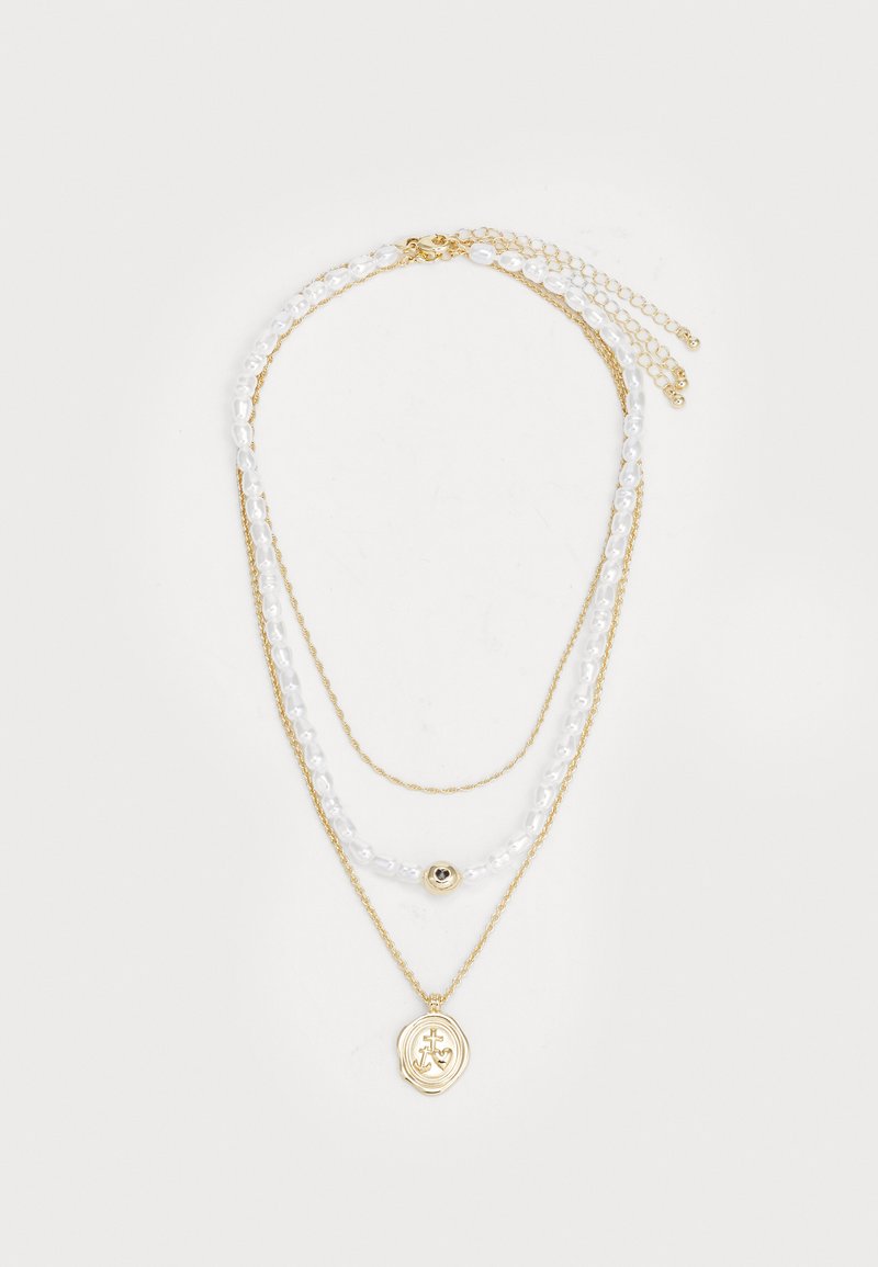 Collar de múltiples capas en oro que presenta cadenas de cuentas blancas, un acento redondo dorado y un colgante dorado con un diseño en relieve.