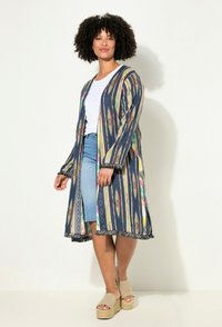 Vícebarevné, vzorované kimono s třásněmi na spodním okraji, dlouhými rukávy a otevřeným předním dílem. Nosené přes bílý top a džínovou sukni, doplněné platformovými sandály.