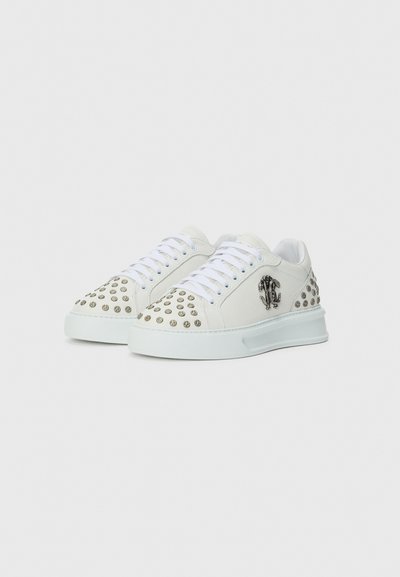 White sneakers with rounded toes, featuring metallic studs on the toe and side, textured material, and flat rubber soles.