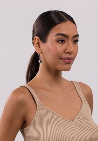 Ohrringe aus Sterlingsilber in Form von Creolen mit einem Sonnenstrahlen-Design, das eine zentrale Perle zeigt. Tragen von einem Modell mit glattem Haar und einem beigen Tanktop.