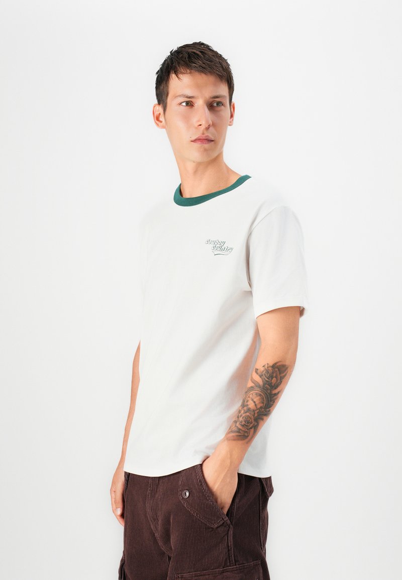 Biała bawełniana koszulka z zielonym ściągaczem przy kołnierzu i małym wyhaftowanym logo. Posiada krótkie rękawy i luźny krój.