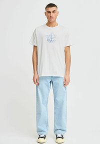 Hvit kortermet T-skjorte med blå grafisk trykk av en seilbåt og tekst. Kombinert med lyseblå rette jeans og svarte sneakers.