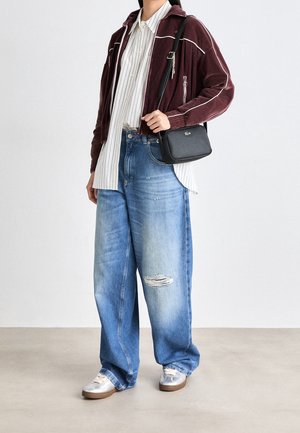 Personne portant une veste zippée bordeaux, un t-shirt blanc rayé, un jean large déchiré, des baskets argentées et un sac bandoulière noir.