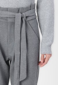 Gray trousers with a wide waistband, featuring a front tie detail and side pockets, paired with a light gray knitted sweater.