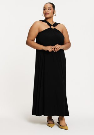 Schwarzes Maxikleid mit Neckholder-Design und einem zentralen Ringdetail. Weicher Stoff fällt glatt bis zum Boden. Mit Schuhen getragen.