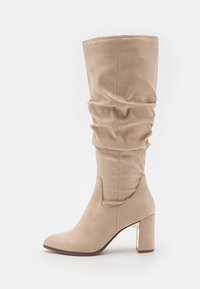 Stivale beige a gamba larga fino al ginocchio realizzato in morbido camoscio, con punta quadrata e tacco a blocco arricchito da un accento dorato.