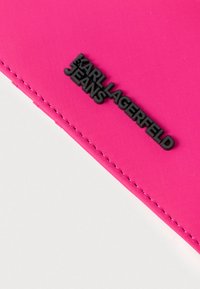 Ružová látková peňaženka s čiernym vyrazeným logom „KARL LAGERFELD JEANS“. Má prešité švy a hladký povrch. Kompaktný obdĺžnikový tvar.