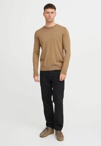 Suéter de punto marrón claro con mangas largas, cuello redondo y dobladillo ajustado, combinado con pantalones negros de pierna recta y zapatos beige.