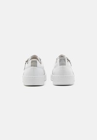 Baskets en cuir blanc avec une finition lisse et des accents gris texturés. Elles disposent d'une semelle en caoutchouc blanc plate et d'un détail de fermeture éclair à l'arrière.