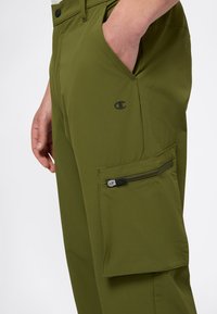 Olivegrüne Cargo-Hosen aus leichtem Stoff, mit einer Reißverschlusstasche an der Seite, zwei Fronttaschen und schwarzem Logodetail.