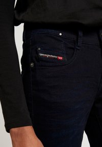 Mörkblå jeans av denim, med en framficka som har en röd och svart Diesel Industry-etikett samt metallhardware-accenter.