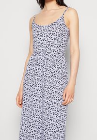 Robe violet clair à imprimé floral noir, bretelles spaghetti, taille froncée et tissu fluide. Design décontracté adapté aux temps chauds.