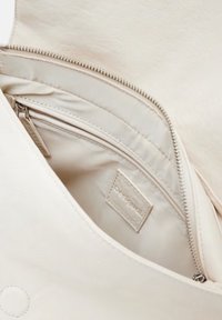 Cremefarbener Handtascheninnenraum mit einer Reißverschlusstasche und einem strukturierten Etikett, mit einem glatten, minimalistischen Design und weicher Stoffauskleidung.