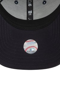 Svart caps med avrundet form, med et sølvfarget klistremerke med et baseball-design på undersiden av sk brim. Teksturert stoff.