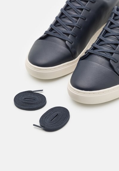 Navy leather sneakers with a rounded toe, white rubber sole, and matching navy laces. Includes an extra pair of navy laces.