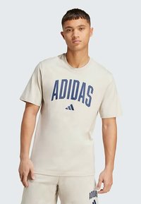 Bežinė krūtinės apykaklės marškinėliai su tamsiai mėlynu "ADIDAS" logotipu. Trumpomis rankovėmis, minkšta medžiaga, laisvas kirpimas, minimalistinio dizaino.