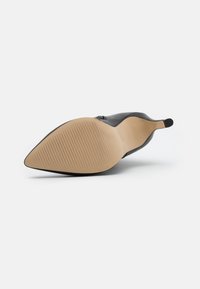 Zapato de tacón alto de cuero negro con puntera afilada, suela texturada y cremallera con acentos dorados a lo largo del lado. Superficie superior lisa.