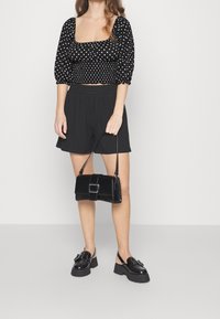 Svart topp med polka prickar och puffärmar, ihop med svarta veckade shorts. Håller en liten svart handväska med kvadratisk spänne. Svarta platåskor.