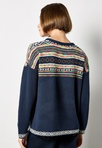 Sweter dziany w kolorze granatowym z teksturowanym wykończeniem. Wielokolorowy, wzorzysty motyw w okolicy dekoltu i przy mankietach, z geometrycznymi wzorami. Luźny krój, okrągły dekolt.