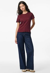 Burgundy ribbad stickad topp med scallopade kanter, ihopparad med vida, mörka denimjeans. Ensamblen har en avslappnad passform och texturerad tyg.