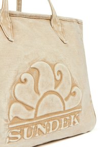 Borsa tote in canvas beige con logo del sole impressa e nome del marchio "SUNDEK" in basso. La texture appare morbida con una leggera lucentezza.