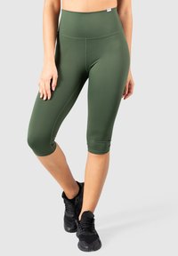 Leggings cropped a vita alta in verde scuro, realizzati in materiale elasticizzato. Presentano una texture liscia e un design aderente. Indossate scarpe da ginnastica nere.